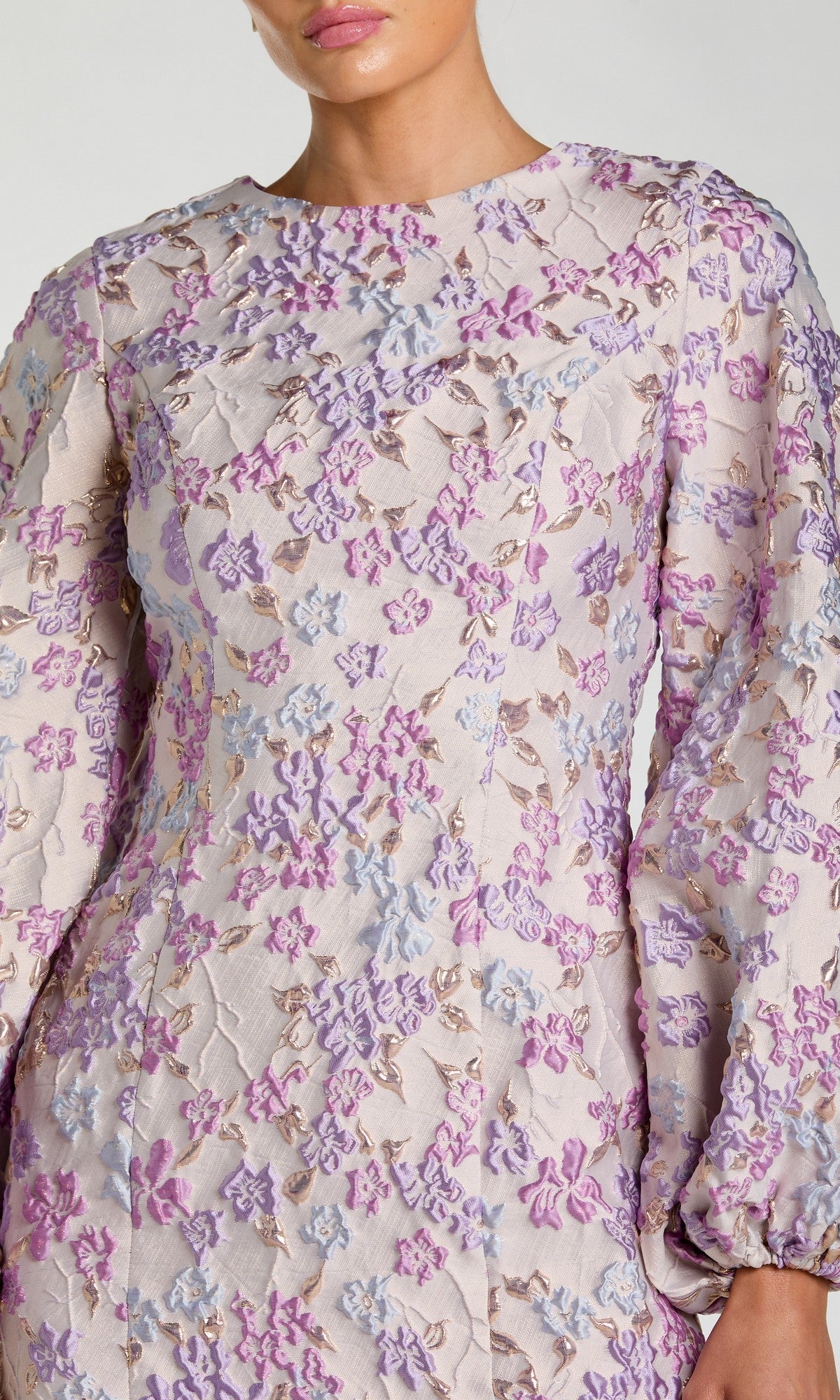 A woman wears the Mac Duggal 56106—a short floral wedding guest dress with long puffed sleeves in purple and lavender—offering a chic, light-colored option for stylish cocktail parties or weddings.